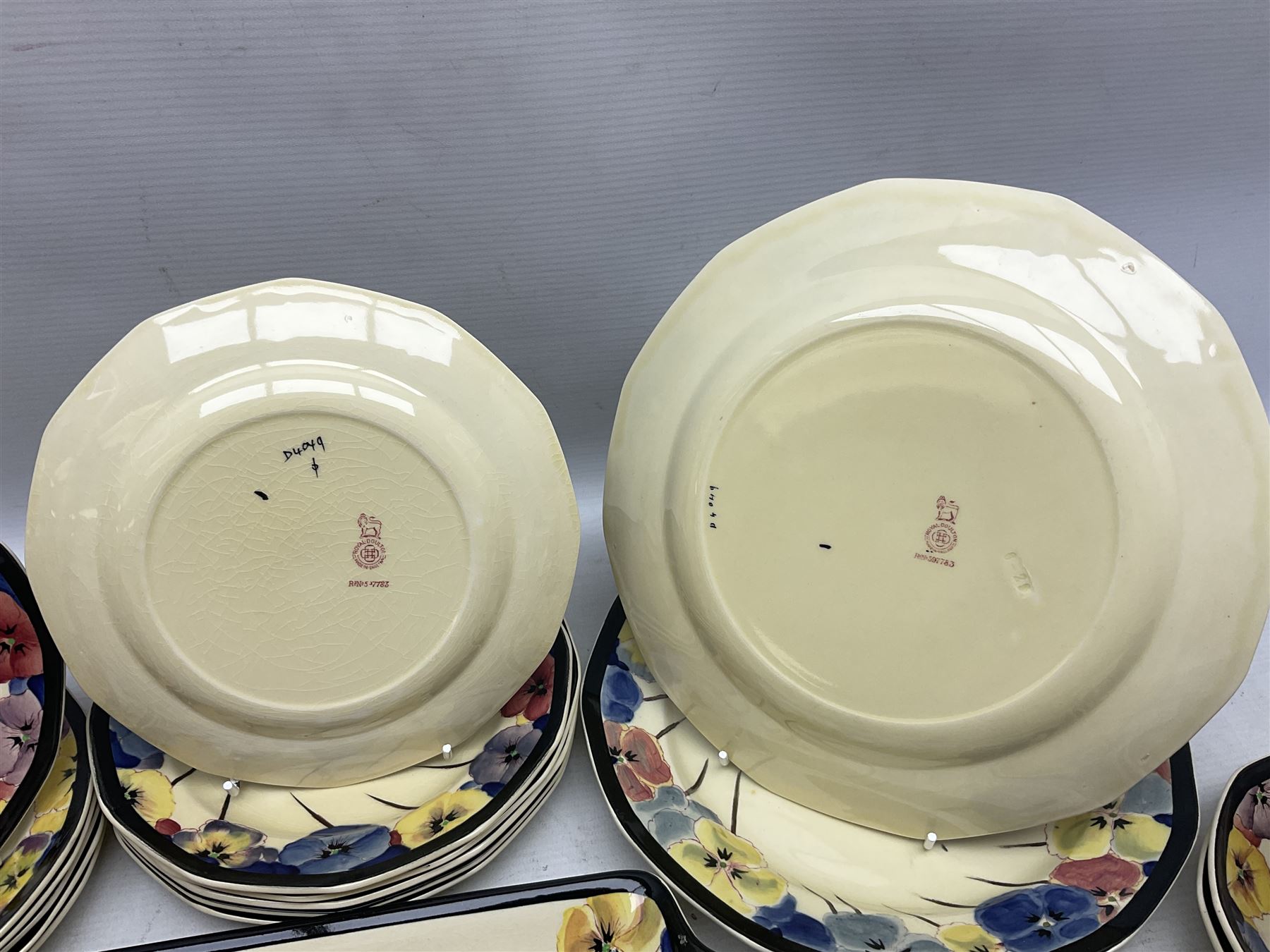 Early 20th century Art Deco Royal Doulton Pansies pattern octagonal teawares, comprising three larger teacups and saucers, three smaller teacups and saucers, open sucrier, two jugs, slop bowl, six side plates, two larger plates, two small circular dishes and one long twin handled rectangular dish, all with printed marks beneath, Rd No 597783, pattern no D4049