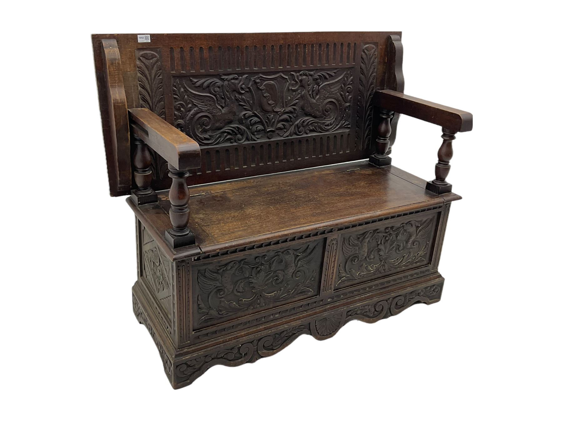 Late 19th century oak monk's bench, the hinged back or top carved with mythical winged dragons, central cartouche and scrolling acanthus leaves, on turned supports, hinged box seat revealing storage, the panelled front matching the back, shaped bracketed skirt carved with shell and scrolled leafage