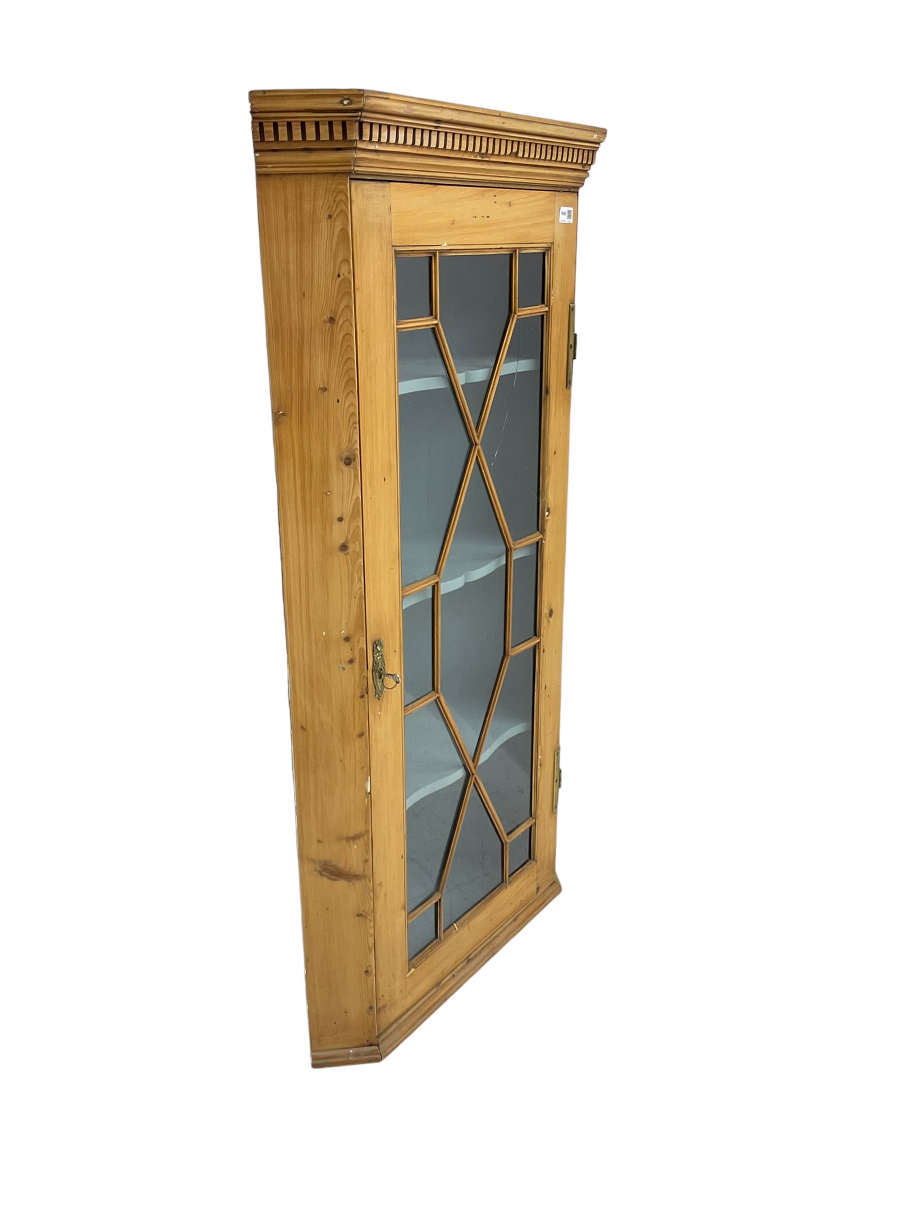 Early 19th century pine corner cabinet, projecting dentil cornice over astragal glazed door