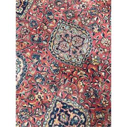 Large Persian design red ground carpet, the field decorated with multiple shaped panels surrounded by trailing leafy branches and stylised plant motifs, the guarded border decorated with shaped panels and floral pattern 