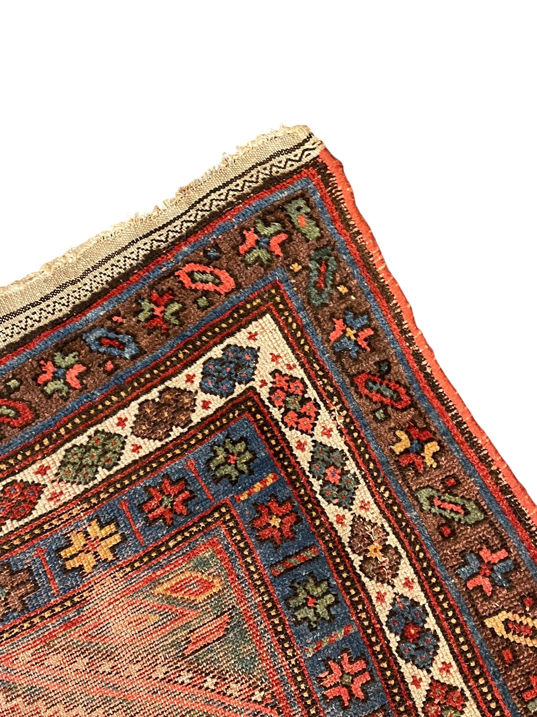 Kurdish crimson ground rug, the field decorated with four lozenge medallions, triple band border decorated with stylised flower heads