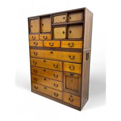 Late Meiji-period Japanese keyaki wood tansu chest, upper section with six sliding woven rattan doors over five drawers, lower section fitted with an asymmetrical arrangement of seven drawers and side cupboard with a hinged door enclosing three additional drawers, iron drop handles to sides