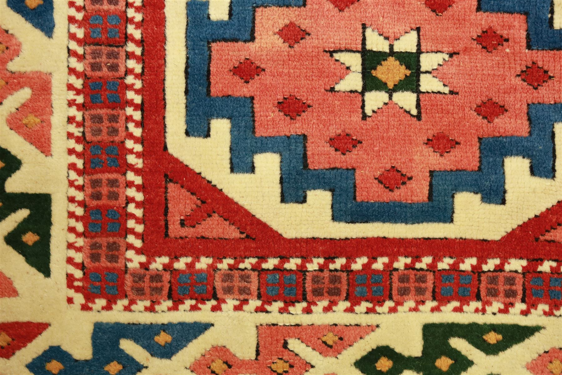 Anatolian Soumak rug, ivory ground decorated with a grid of eight octagonal medallions in terracotta red outlined in blue, centered with a star motif in vertical rows, framed by a series of geometric borders in ivory, green, and blue, incorporating hooked devices and stylized lozenges and stripped end panels, with signature at either end 