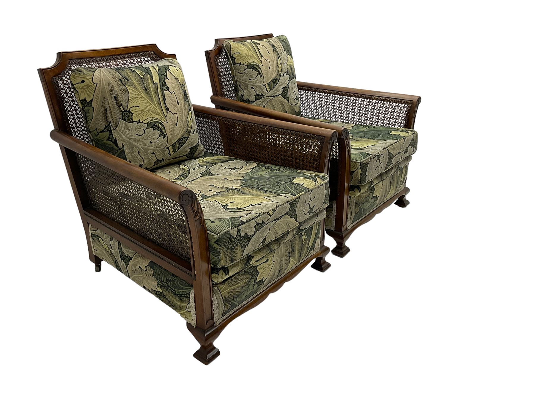 Early 20th century bergère lounge suite, mahogany framed with cane work back and sides, acanthus scroll carved uprights - three seat sofa (W167cm, H82cm, D83cm), and pair matching armchairs (W78cm), loose cushions upholstered in acanthus leaf scroll fabric with scatter cushions