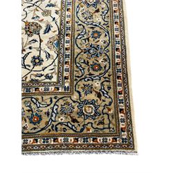 Persian Kashan ivory ground carpet, overall floral design, the field decorated with scrolling and interlaced leafy branches interspersed with palmettes, scrolling border decorated with stylised plant motifs, within floral pattern guard stripes 