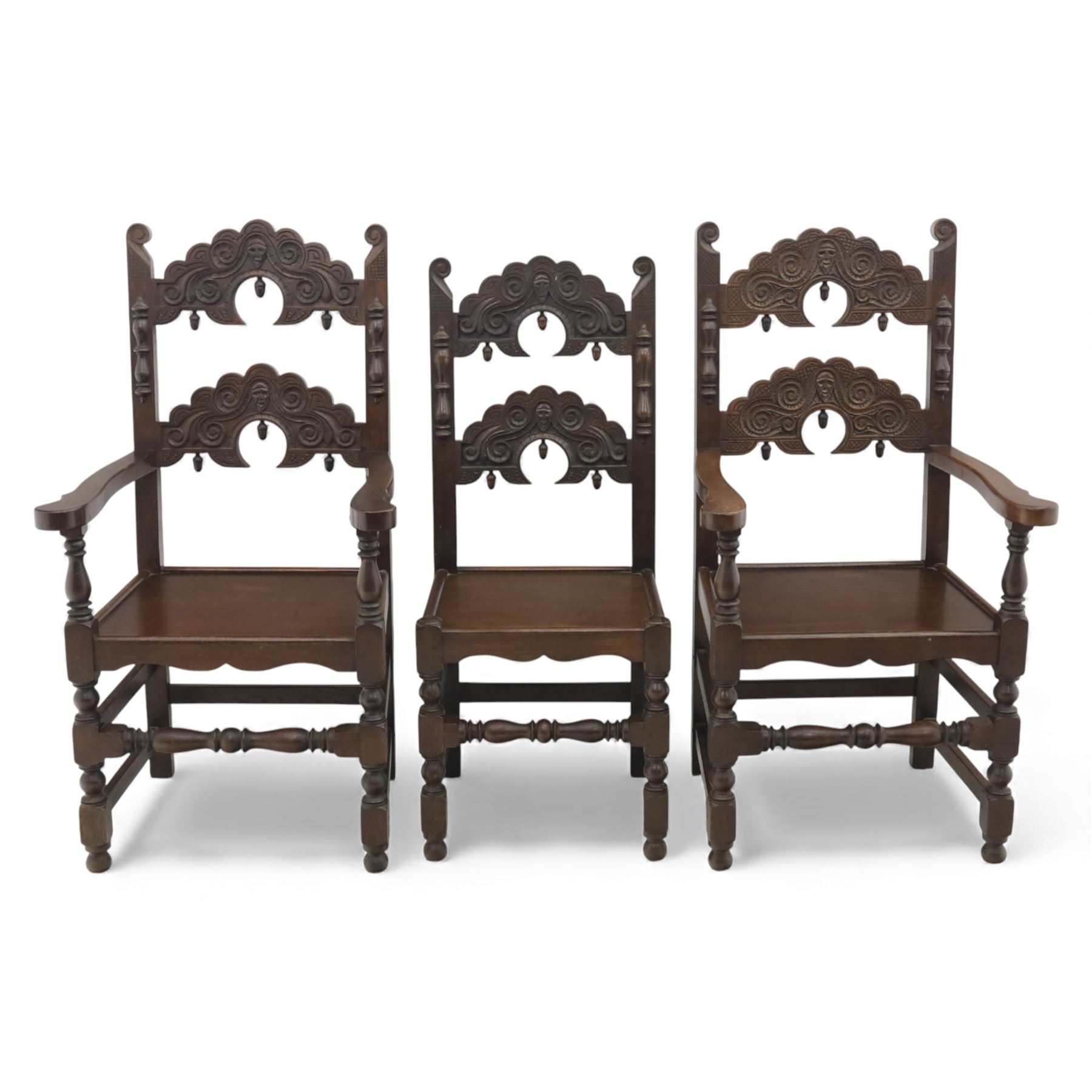 Early 20th century set of seven Jacobean Revival oak chairs, comprising pair of cavers and five chairs, each with carved mask and scroll decoration to the crest and and back rail, plain oak seat, upon turned front legs and block rear legs with conforming stretchers