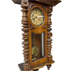 1890’s German striking wall clock in a walnut case, striking the hours and half hours on a coiled gong, eight-day Juhngans movement with a two-part dial, Roman numerals, gothic steel hands and visible gridiron pendulum, case with turned pilasters, applied carving and glazed full length door.

