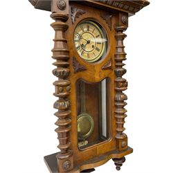 1890’s German striking wall clock in a walnut case, striking the hours and half hours on a coiled gong, eight-day Juhngans movement with a two-part dial, Roman numerals, gothic steel hands and visible gridiron pendulum, case with turned pilasters, applied carving and glazed full length door.

