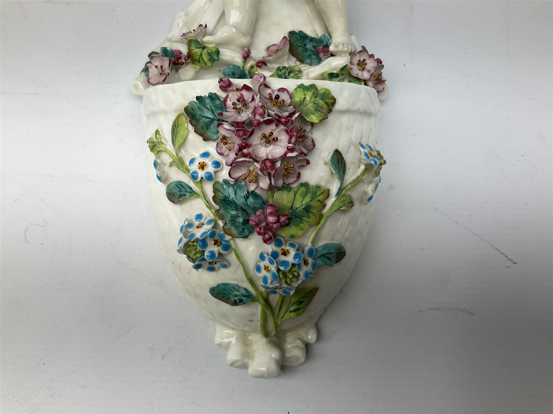 Victorian wall pocket by Moore Brothers retailed by T.Goode modelled as a semi nude white glaze cherub with turquoise ribbon, with encrusted floral decoration, the reverse stamped ‘T.Goode & Co.’, H32cm