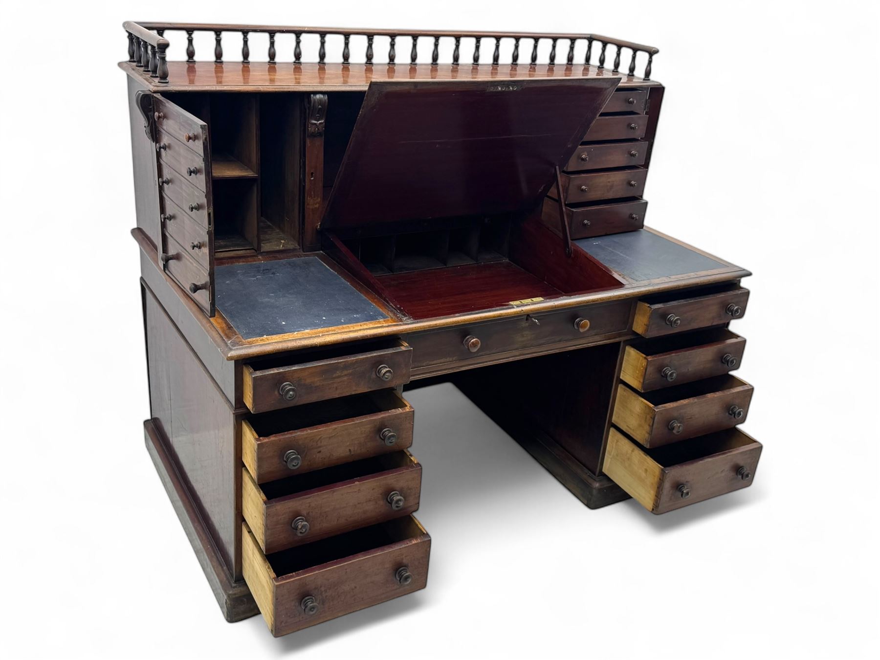 Large Victorian mahogany Registry/Dickens’ desk, spindle gallery top, one side with five small drawers and the other with blind cupboard drawer, revealing pigeon holes with scroll carved locking side bars on either side, above a hinged and leathered writing slope with three drawers and pigeon holes underneath, above a central locking drawer with key, the pedestals each with four drawers and  turned knob handles, separates into four parts for transport