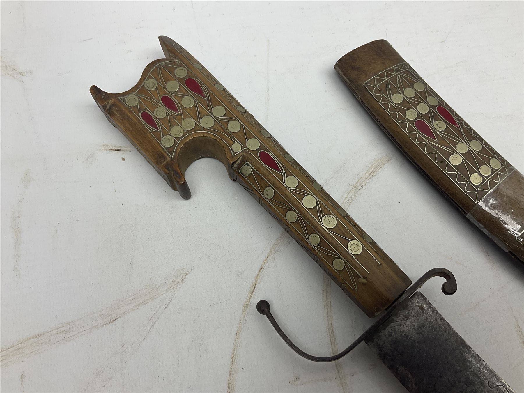Late 19th/early 20th century Moroccan nimcha dagger-sword, the 40cm curving steel blade with engraved decoration on both sides; shaped hardwood hilt inlaid with brass, white metal wires and red coloured panels; in similarly inlaid scabbard L61cm overall