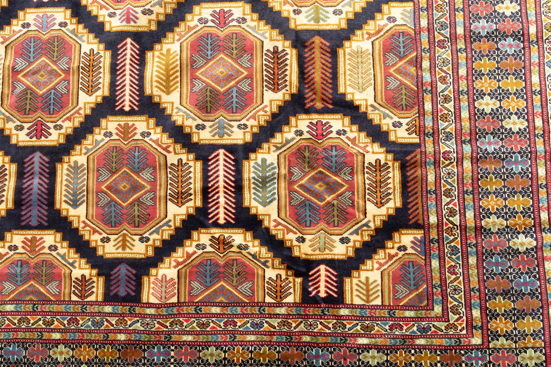 Central Asian Turkmen, main field with octagonal guls enclosing hooked diamond motifs in shades of madder gold, ivory, and indigo set against a dark ground within multiple polychrome borders of geometric devices and stepped motifs 