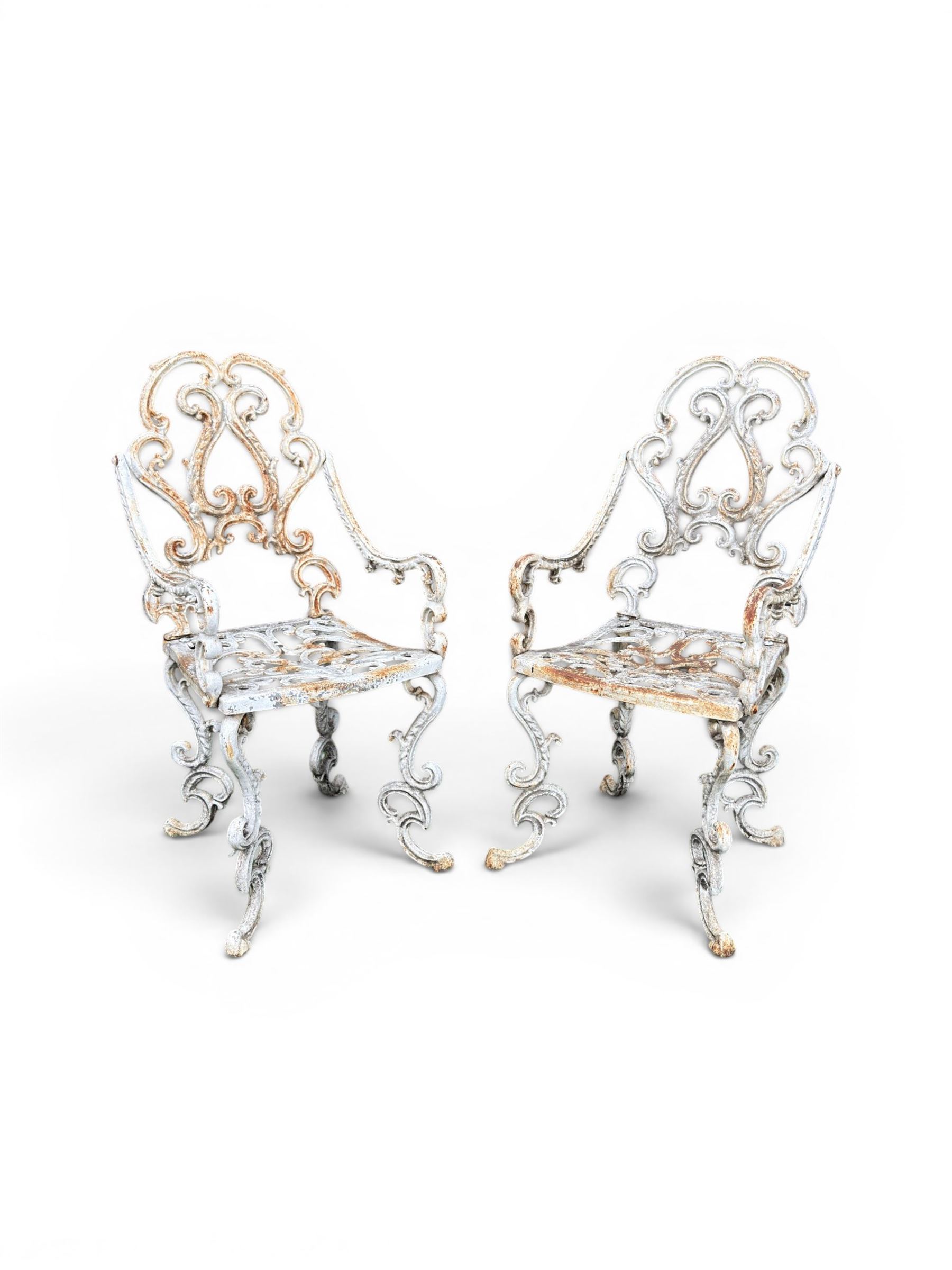 Pair of Victorian cast iron garden chairs, the ornate pierced back of scrolling foliate design, scrolling arm terminals over splayed supports formed of C and S-scrolls, in distressed white painted finish