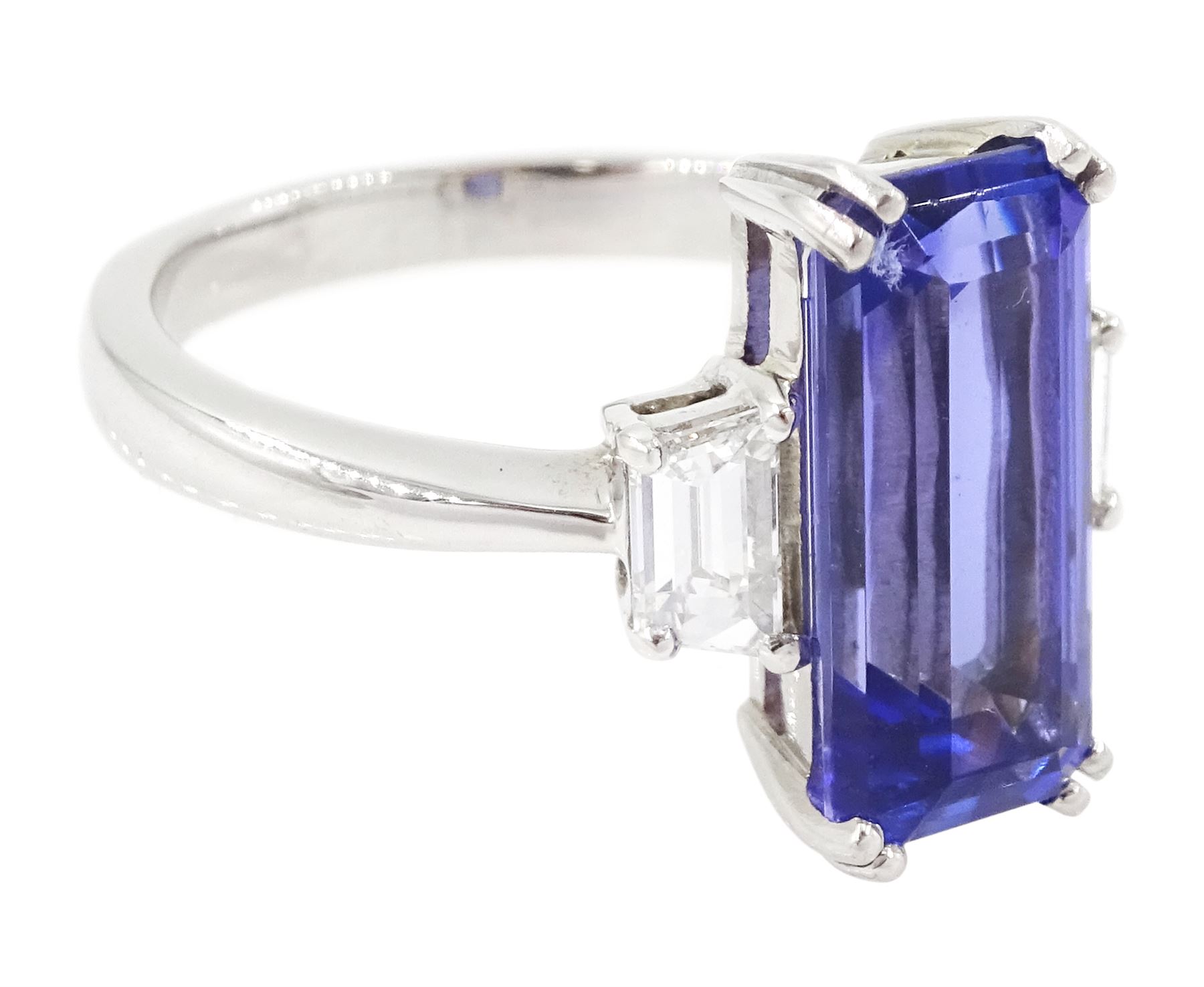 Platinum tanzanite and diamond three stone ring, single emerald cut tanzanite of approx 4.20 carat, with with a single trapeze cut diamond set either side, stamped PT950, total diamond weight approx 0.49 carat, with Alan Poultney Gems report