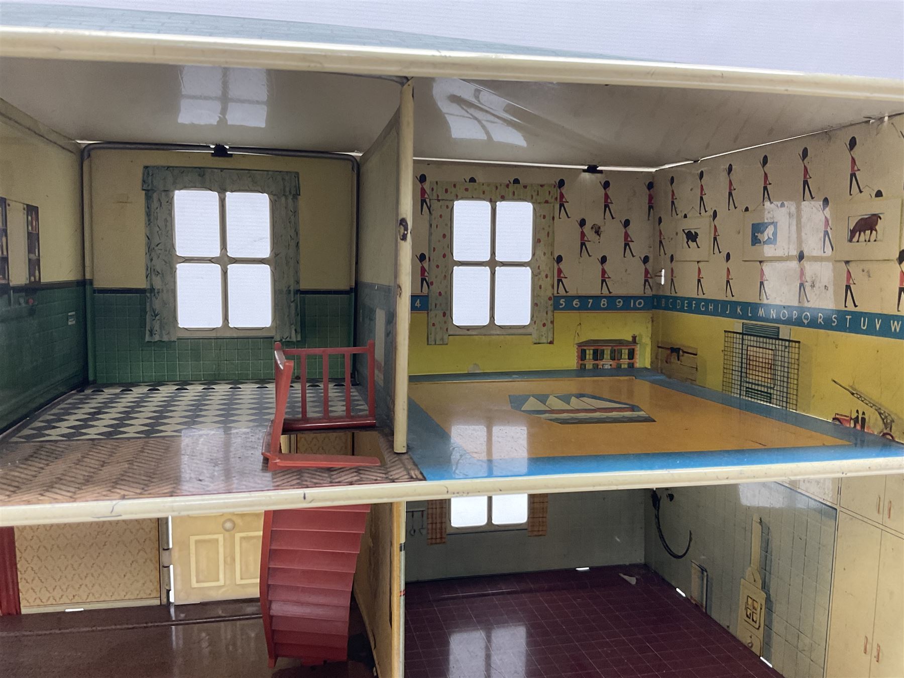 Mid-20th century Mettoy tin-plate double-fronted two-storey doll's house, the front elevation with five unglazed windows flanked by green shutters, central opening door, open back giving access to five rooms together with an attached garage, 60cm wide
