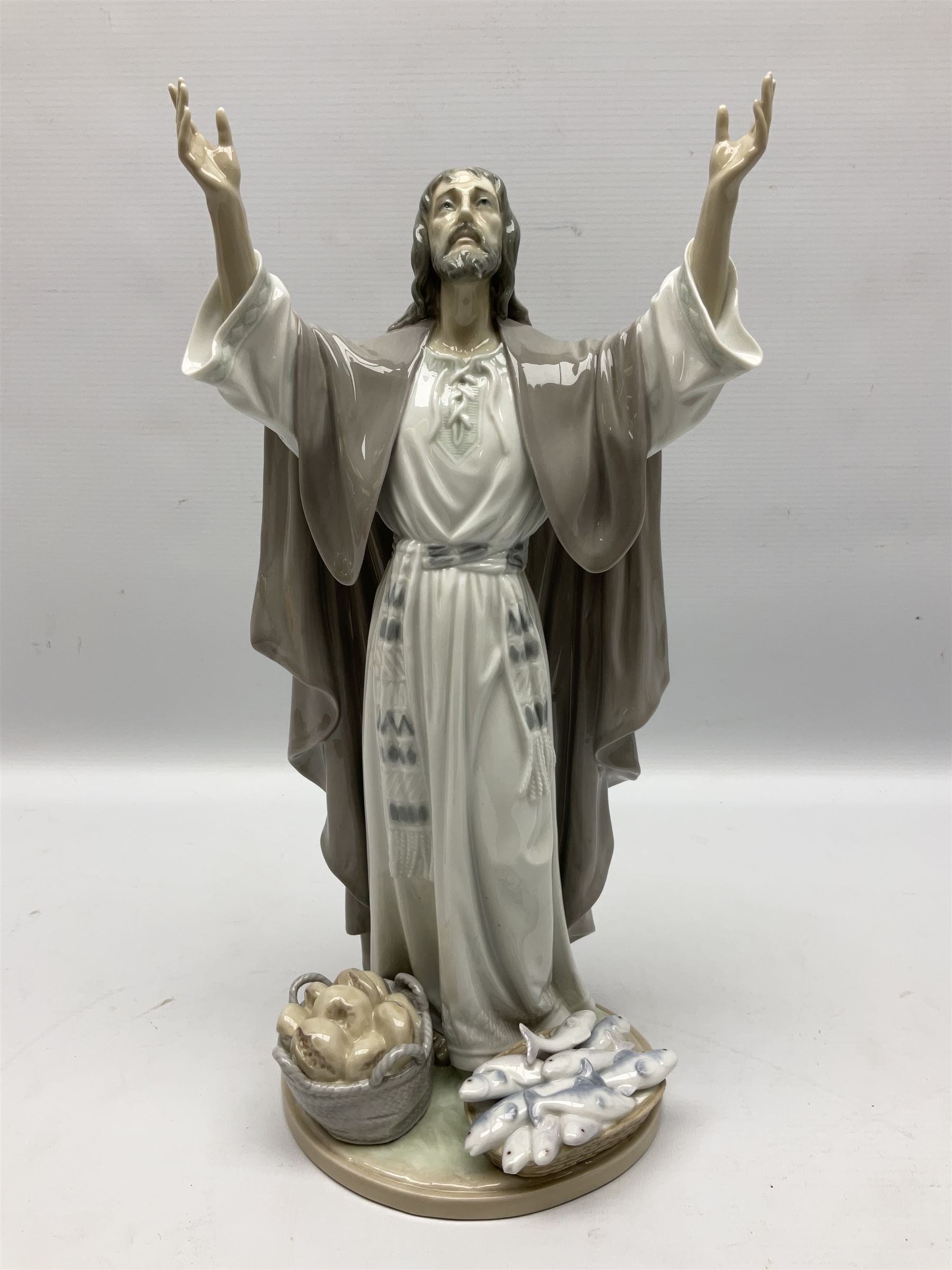 Lladro figure, The Loaves and Fishes, modelled as Jesus Christ with arms raised standing beside a basket of loaves and a basket of fish, sculpted by Salvador Furió, with original box, no 5896, year issued 1992, year retired 1997, H35cm
