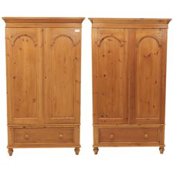 Two contemporary traditional-style wardrobes, projecting plain cornice above two arched moulded panel doors, above a full-width drawer fitted with turned wooden handles, raised on turned bun feet