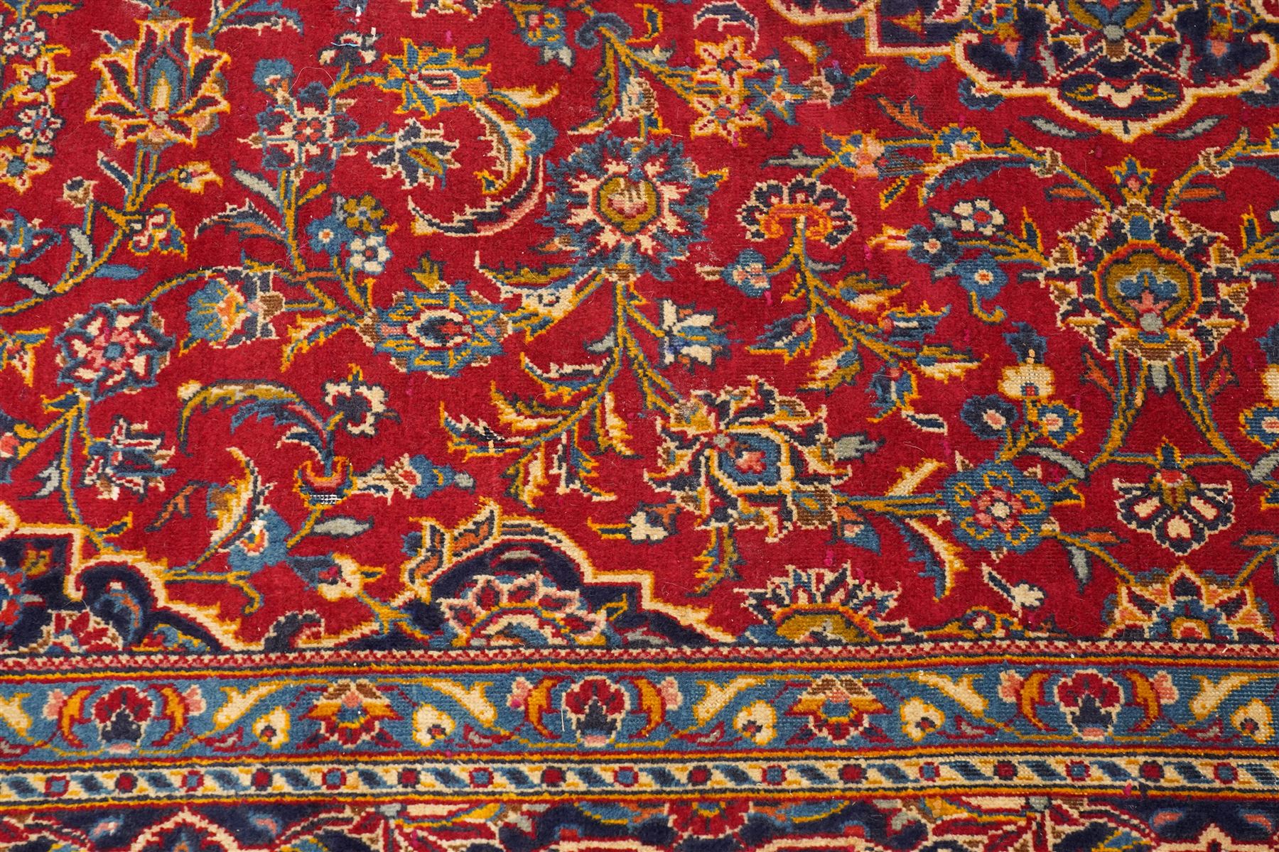 Persian Kashan hand-knotted carpet, madder red ground centred by shaped dark navy, ivory and pale blue floral medallion with pendants, surrounded by scrolling vines, palmettes and flowerheads, dark navy spandrels, enclosed by dark navy floral border with multiple floral guard stripes