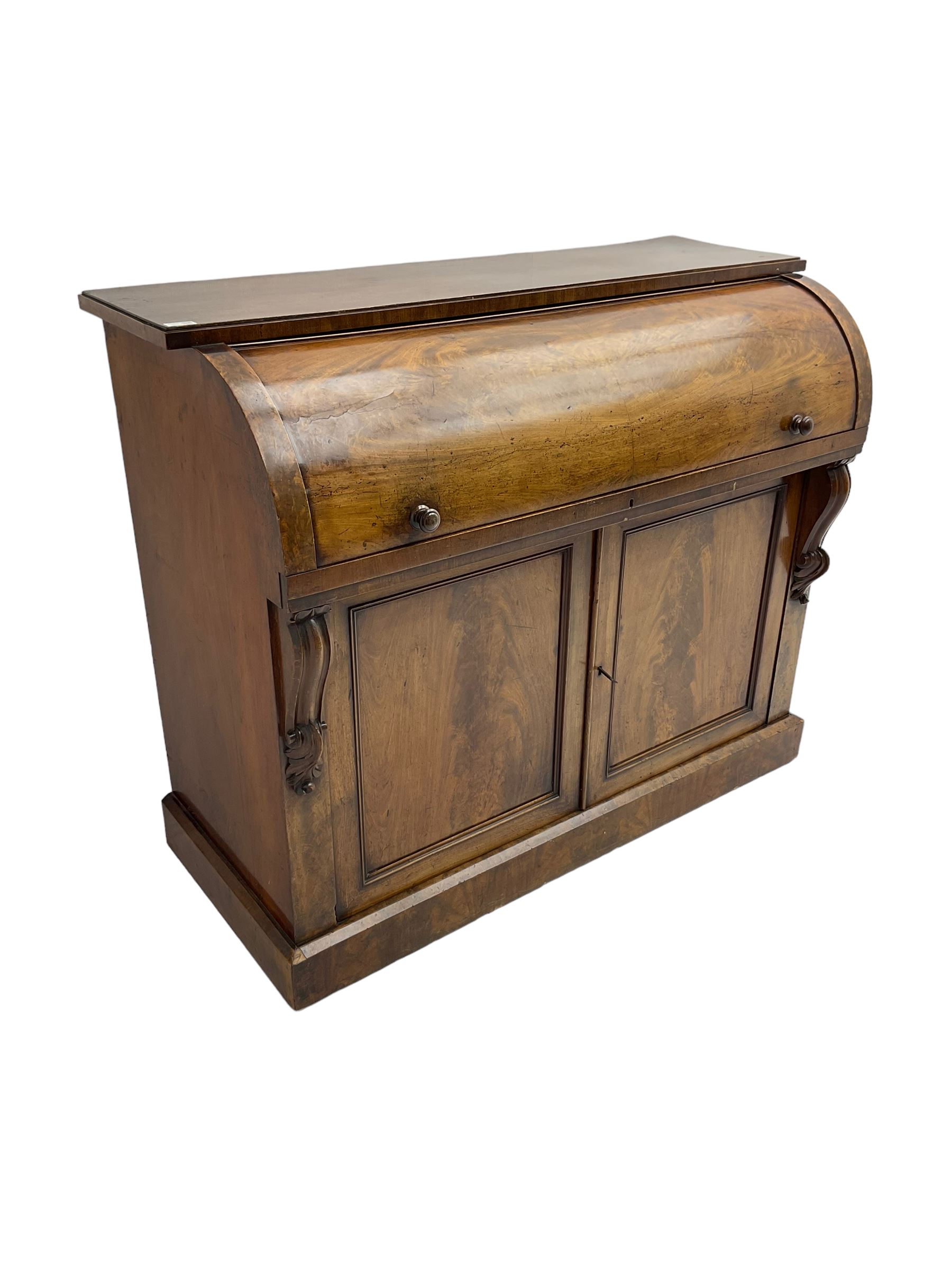 Victorian mahogany roll-top writing desk, top concealing fitted interior with pigeonholes and three drawers, the trisector inset writing surface with writing slope, base fitted with panelled cupboard enclosing single shelf, decorated with scrolled corbels