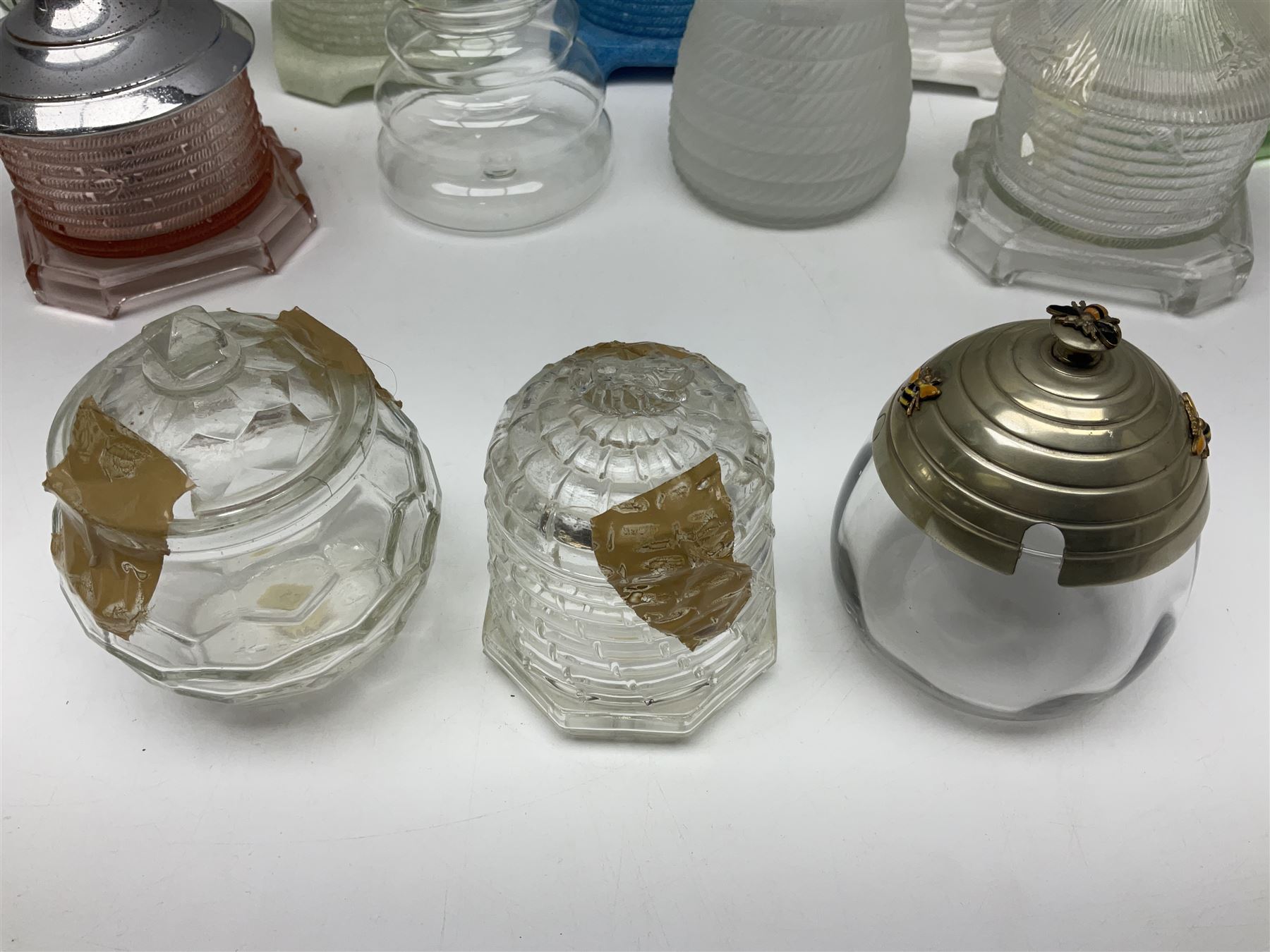 Collection of glass beehive honey pots, to include a blue slag example, milk glass, pink, green, etc together with four white metal examples (16) 