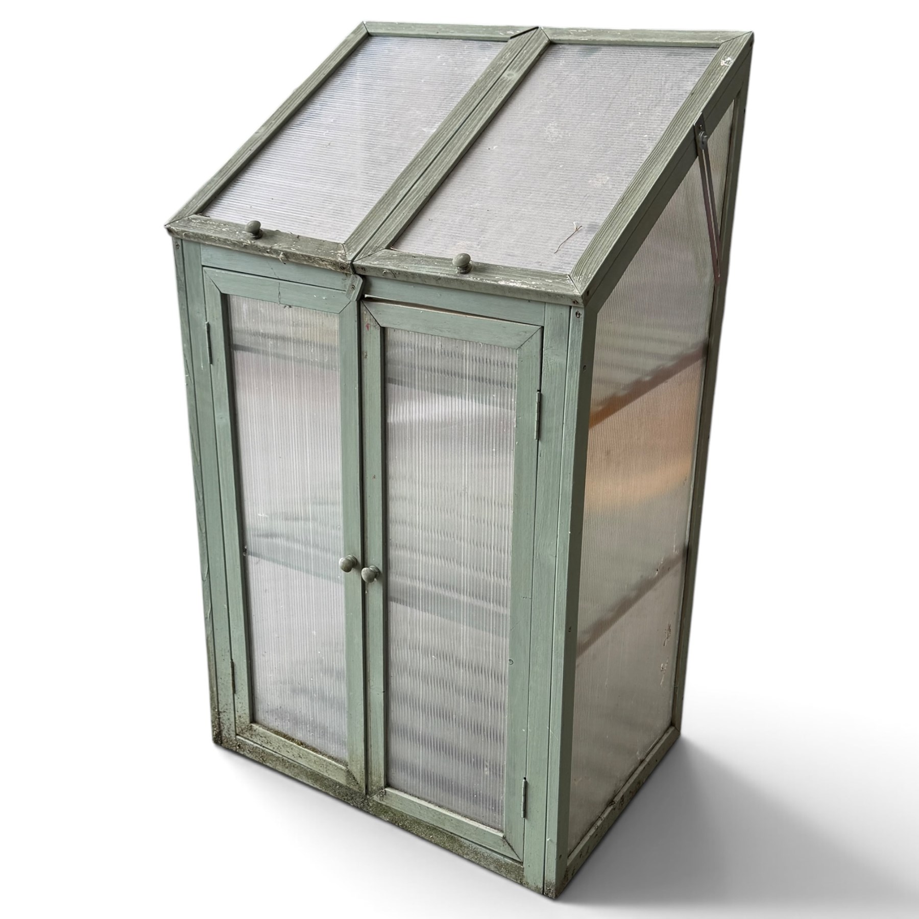 Three green-painted timber cold-frame greenhouses or growhouses, each with twin hinged sloping polycarbonate lids above a pair of panelled doors enclosing slatted shelves
