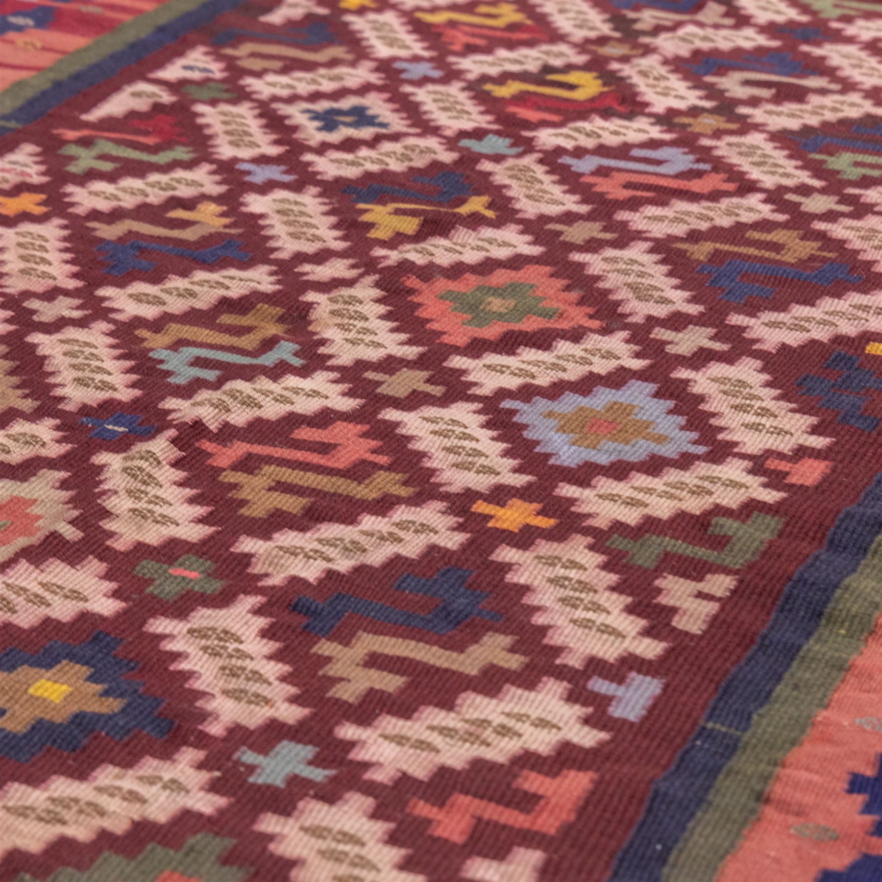 South West Persian Qashgai flatweave kilim, field decorated with a repeating diagonal lattice of stepped lozenges and angular hooked motifs, interspersed with small tribal devices, woven is shade of madder red, soft pink, indigo blue, ochre, and olive green, framed by a narrow geometric border and contrasting guard stripes 