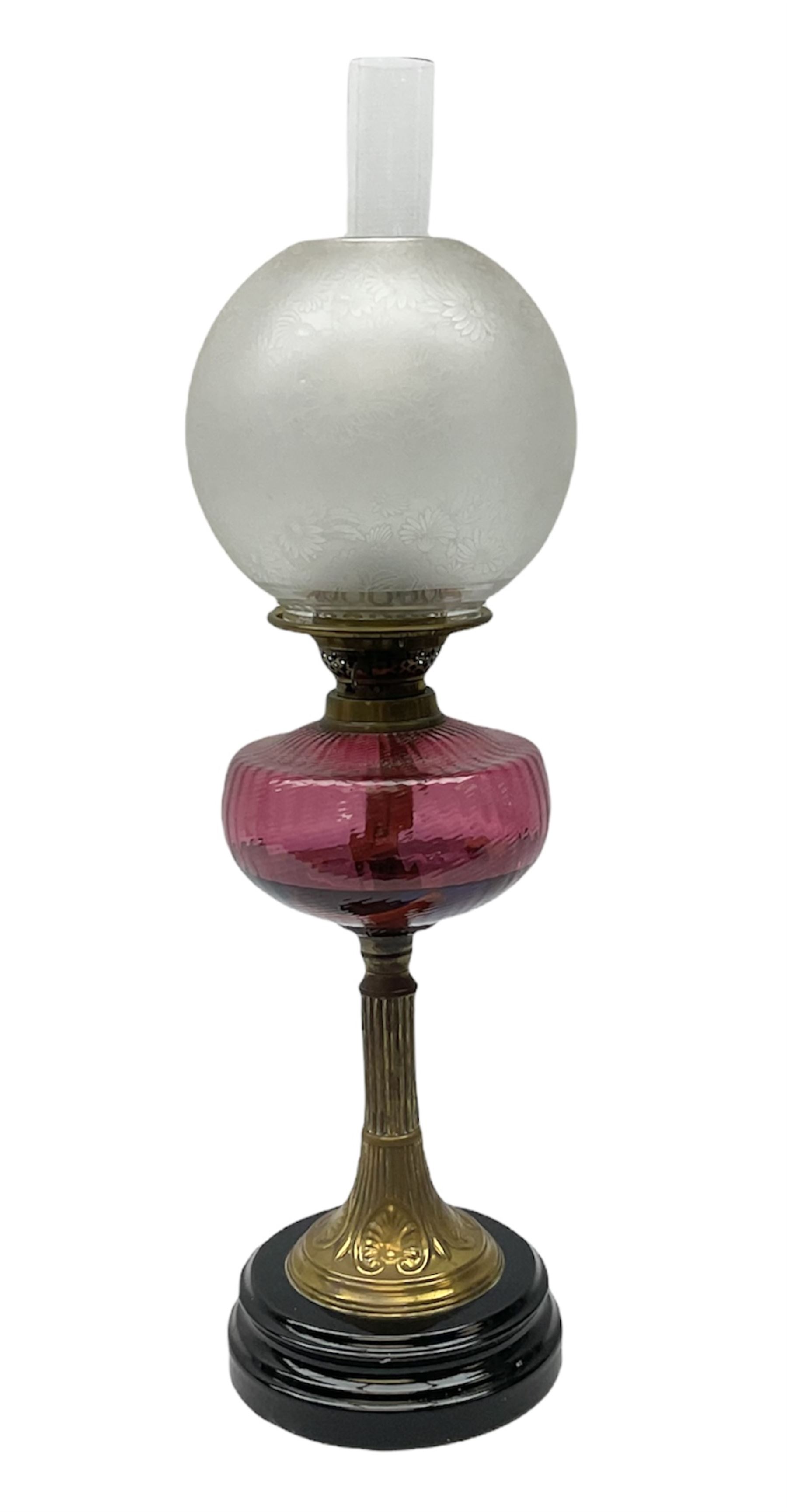 Victorian table standing oil lamp, brass fittings, cranberry glass reservoir, brass column on black enamelled ceramic base, with a frosted glass shade and clear glass chimney, H68cm