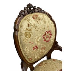 Pair of Victorian lady's and gentleman's walnut open armchair and nursing chair, shaped cresting rail carved with scrolls and flower head, upholstered in pale gold fabric decorated with floral pattern, foliate carved cabriole feet, on brass and ceramic castors 
