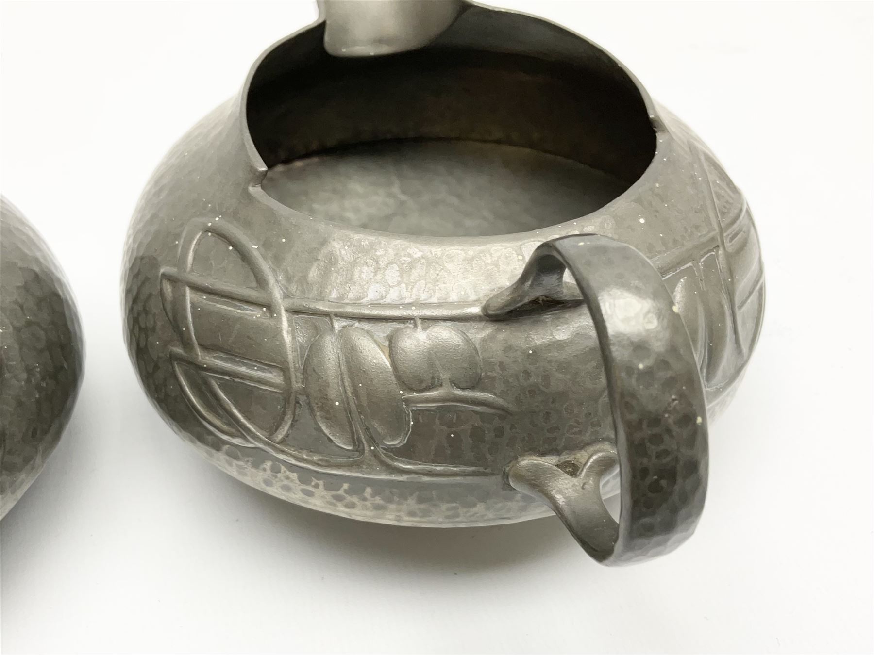 Archibald Knox for Liberty & Co Tudric pewter three piece tea service, comprising teapot with woven reed handle, single handled open sucrier, and milk jug, each with planished finish and detailed with honesty flowers, each impressed beneath Made in England Tudri Pewter 0231 