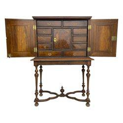 19th century walnut collector's cabinet on stand, the moulded top over two figured doors with arched ebony stringing, the interior fitted with various drawers and central cupboard, the figured drawer fronts with moulded ebonised borders and foliage cast gilt metal loop handles,  the stand with moulded top rails over turned supports, cusped lower rails with central finial, on turned feet