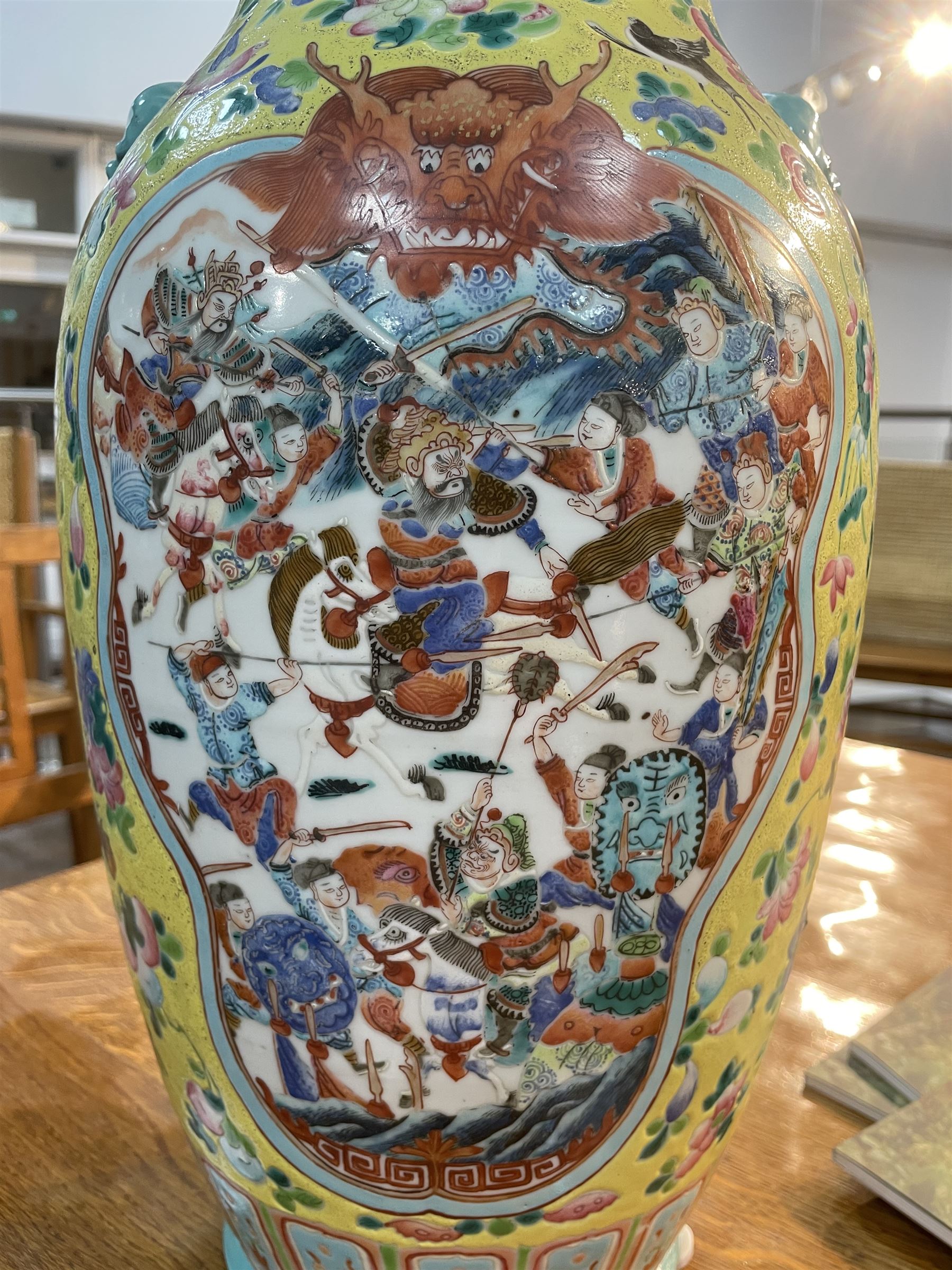 19th century Chinese famille rose yellow ground porcelain vase, of baluster form with twin applied mask ring handles, the body decorated with two shaped reserves mounted with dragon heads, depicting warriors at battle and at court, the neck with two smaller conforming figural reserves, upon a yellow ground decorated with exotic birds amidst scrolling blossom, H45.cm