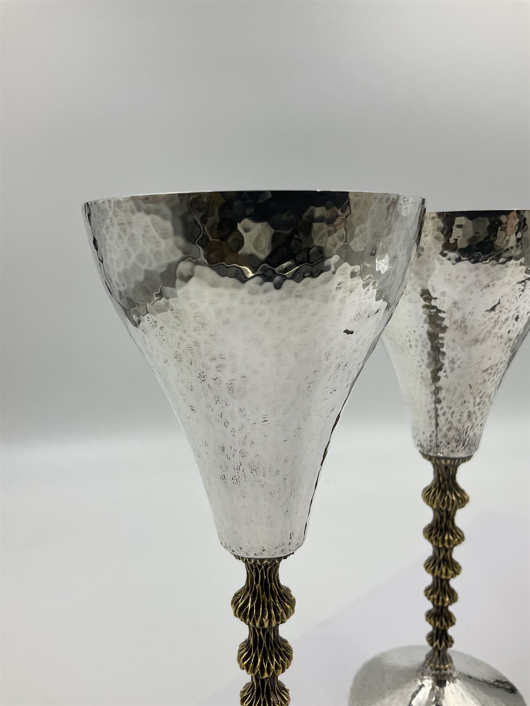 Pair of modern silver goblets by Stuart Devlin, the tapering cylindrical bowls each with spot hammered decoration and gilt interiors, the parcel gilt stems with signature textured detailing and six graduating knops, upon conforming spreading circular foot, hallmarked Stuart Devlin, London 1976, H17.7cm