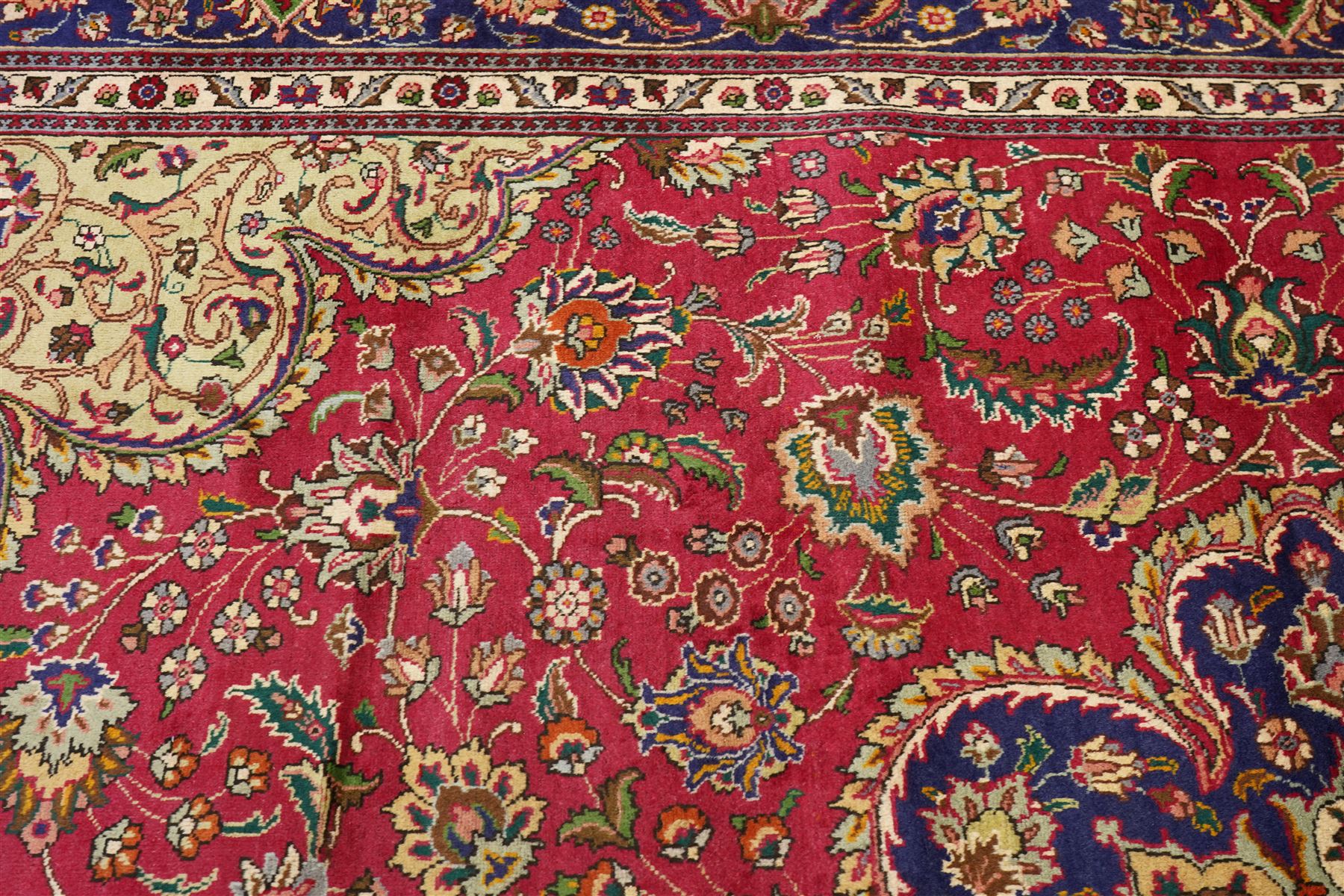 North East Persian Meshad hand-knotted carpet, crimson field with central lobed medallion in tones of indigo, ivory and soft blue, with an all-over arrangement of scrolling vinery, palmettes, and floral  sprays, conforming spandrels, main border of stylized floral vinery framed by multiple guard borders, with cotton fringe ends