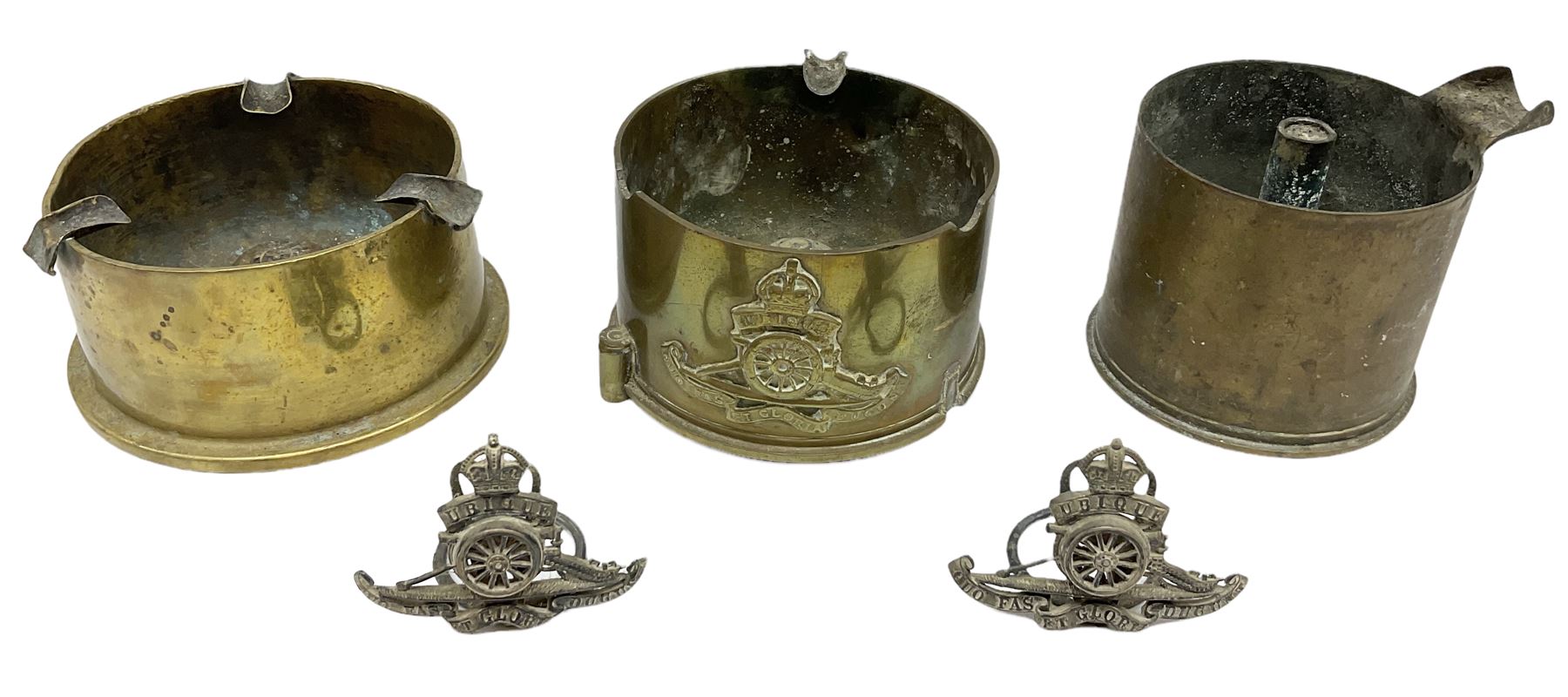 Trench Art - three WW2 brass shell case ashtrays, one mounted with Royal Artillery cap badge and button and one mounted with RA button; together with a pair of place name holders each formed from a Royal Artillery cap badge (5)