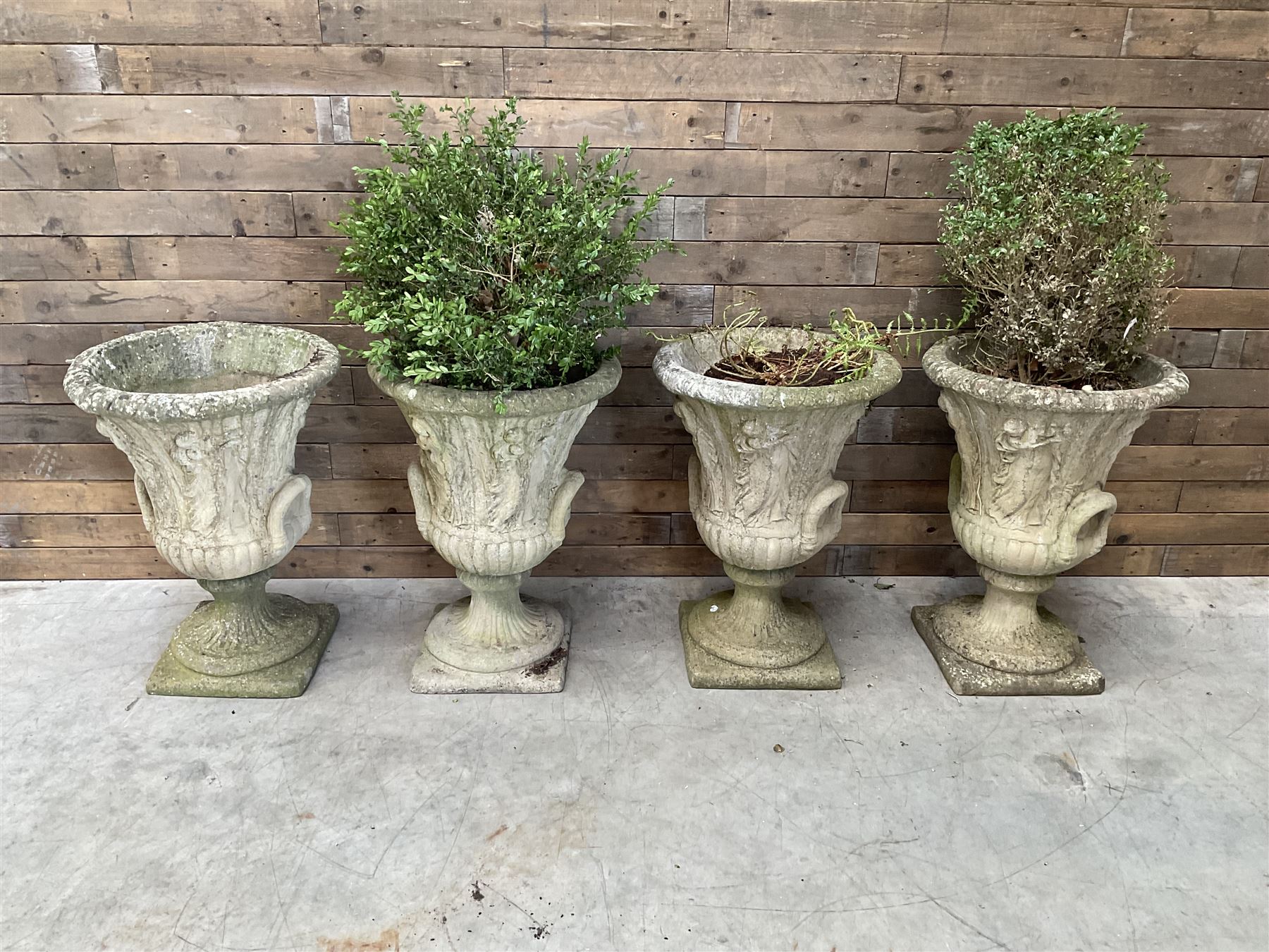 Set of four Victorian design cast stone Grecian urns, tapering form cast with figures and handles, square plinth bases