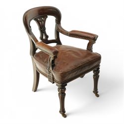 Victorian mahogany library elbow chair, arched cresting rail over shaped and pierced splat carved with cartouche, upholstered arms and seat in brown leather with studded bands, turned and lobe carved front supports on brass and ceramic castors 