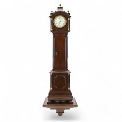 Early 20th century - mahogany cased 8-day miniature longcase clock with a matching wall mounted bracket,  break arch hood with ball finials and recessed quarter pilasters, conforming trunk with a long door and break arch top on a decorative plinth with a raised panel and stepped base, circular dial with Roman numerals and spade hands within a glazed bezel, French insert timepiece movement with a cylinder platform escapement, wound and set from the rear. With key.