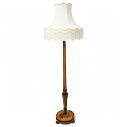 20th century walnut standard lamp, flared and faceted column over circular stepped base with shaped feet, with later scalloped cream fabric shade and fringe trim