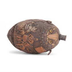 Early 19th century carved coconut 'bugbear' flask, carved with circular panel of Justice stood by a vacant oval shield, holding scales and sword aloft, and stood upon a serpent, and a vignette carved with figures in merriment, drinking and playing music, with profusely carved foliate detail to the rest of the body, the top carved with typical grotesque face with inset glass eyes, and metal nozzle mouthpiece, including mouthpiece L17.5cm 

