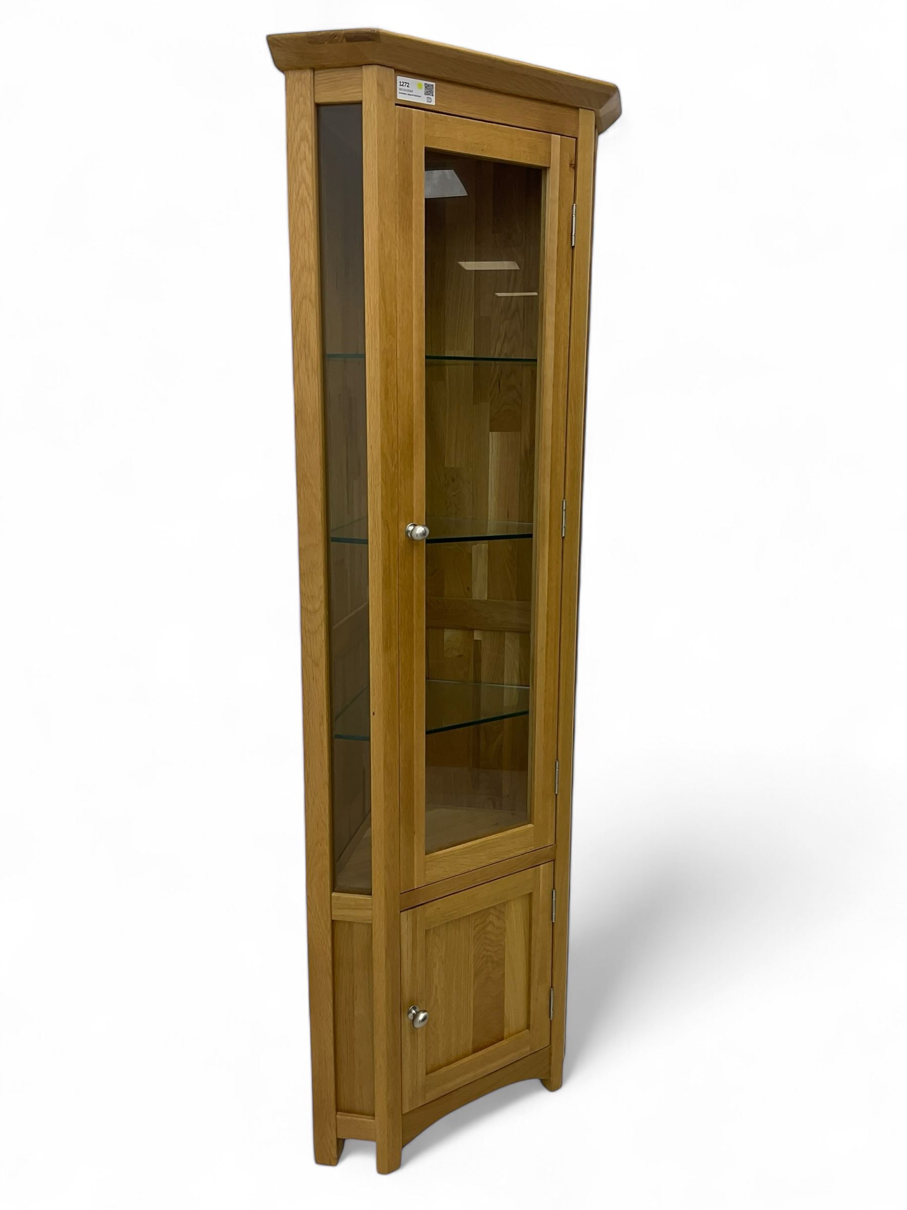 Contemporary light oak corner display cabinet, projecting cornice over single glazed door enclosing three glass shelves, the base fitted with panelled cupboard enclosing single oak shelf, on stile supports