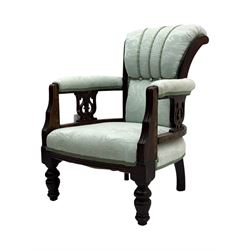 Late Victorian carved mahogany open armchair, the shaped back with fluted upholstered panel and padded arms above pierced scroll carved side supports, over a broad upholstered seat, on turned front supports