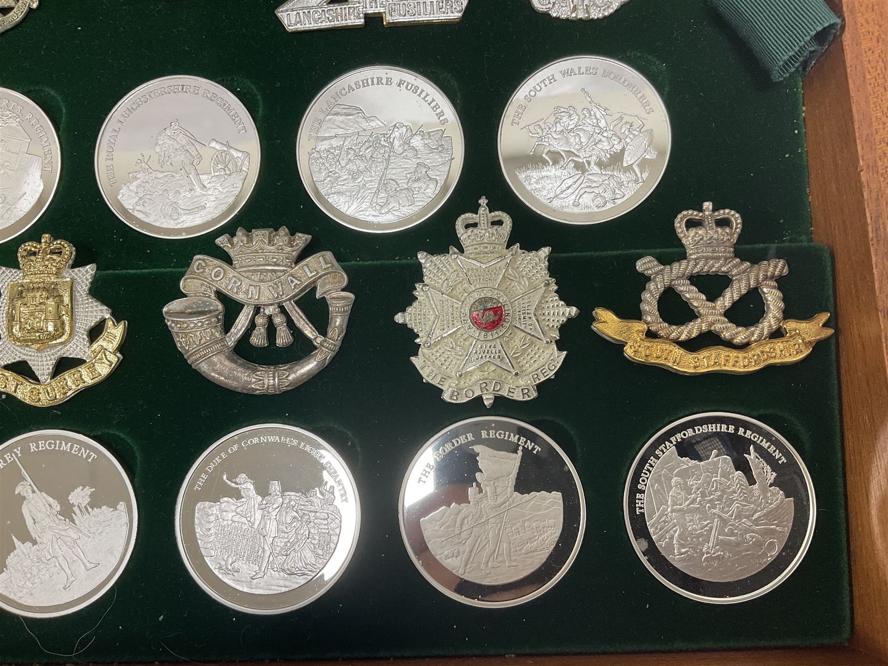 Great British Regiments, 1977, set of fifty two frosted silver medals by the Birmingham Mint, each bearing the name of a regiment with a depiction of an action on the obverse and further details on the reverse, all hallmarked Birmingham Mint, assay offices and dates; together with 52 base metal copy cap badges for each regiment, all housed and mounted on two trays and contained within a wooden presentation case, with brass plaque and fittings, lock and key, with a certificate of authenticity 