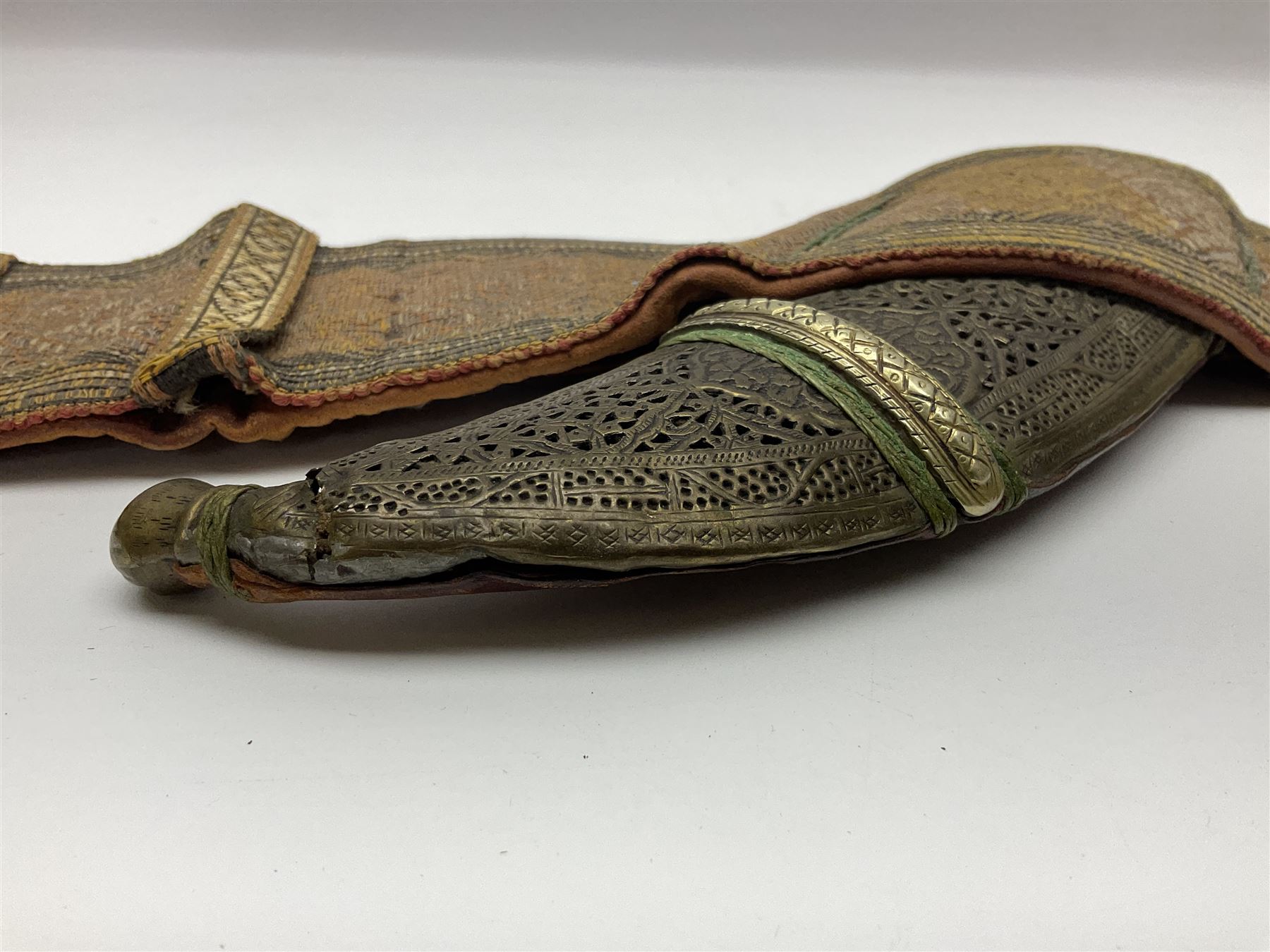 Late 19th century Yemeni Tuza jambiya as worn by religious elite, the 20.5cm curving blade with raised medial ridge, the horn hilt with pique style studwork, in a leather wrapped wooden scabbard with pierced metal mount and leather belt applied with embroidered 'gold' and 'silver' thread work panel; dagger L36cm overall, belt L84cm