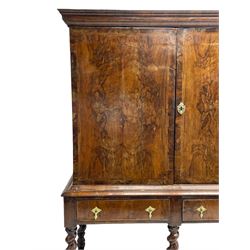 George II walnut cabinet on stand, the moulded projecting corner over two doors with quarter-matched veneered doors, the interior fitted with shelves, the stand with moulded upper rails over two drawers, on a series of spiral turned supports with shaped waved stretchers, on turned feet
