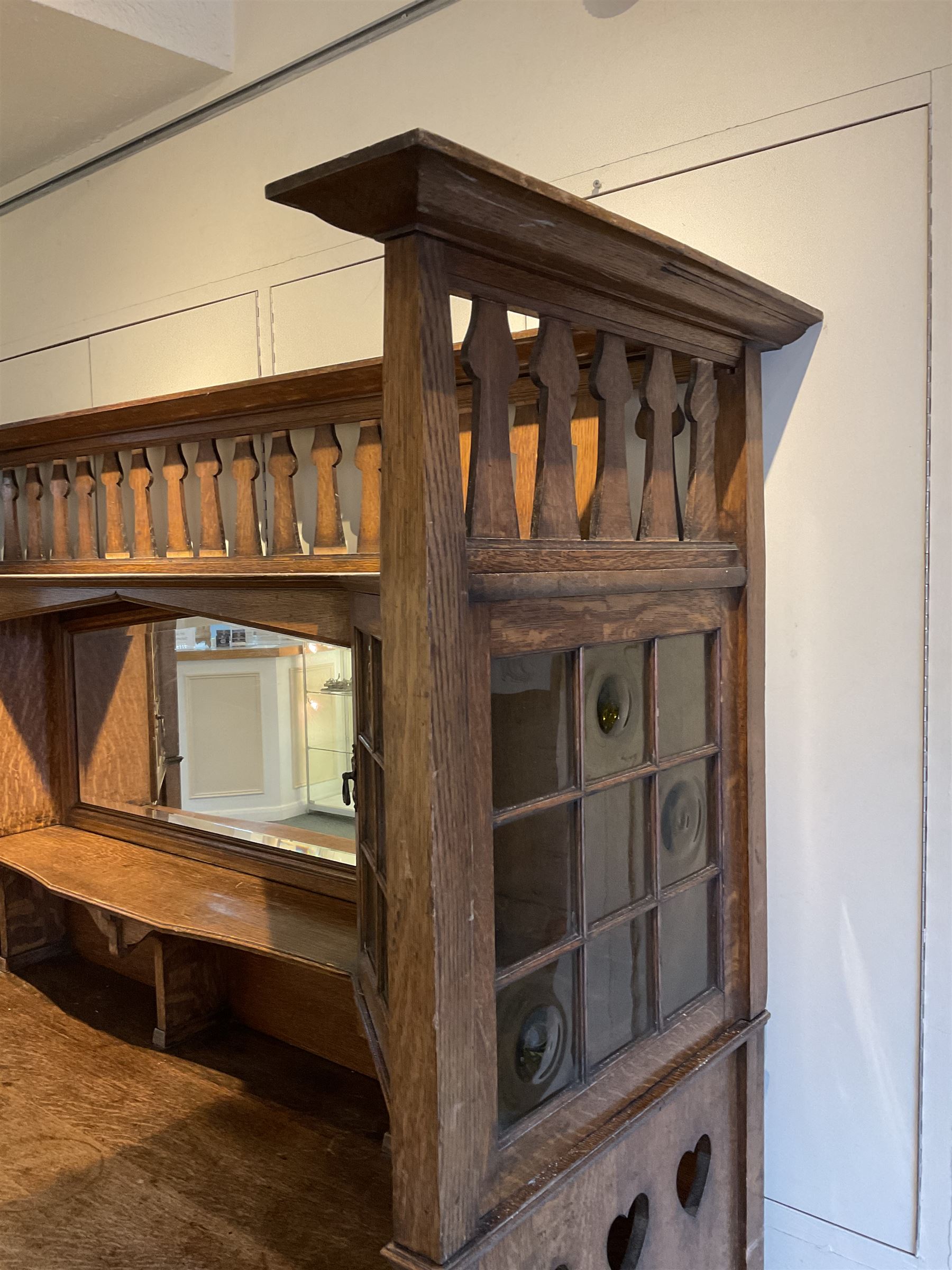 Shapland and Petter - Arts & Crafts period oak dresser, raised gallery top with spade balustrade, central bevelled mirror flanked by two cabinet, astragal glazed doors with yellow tinted glass and bullseye panes, the sides with pierced heart shaped decoration, fitted with two drawers and two double cupboards, enclosed by linenfold panelled doors,  copper work strap hinges and fixtures, on shaped spade feet, the locks stamped 'S&P'
