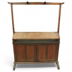 Early 20th century oak saddle and tack stand, the sloped top section for saddle storage raised on rectangular panelled base with cupboard doors enclosing shelved interior, with integral upright frame and horizontal rail fitted with three curved tack hook