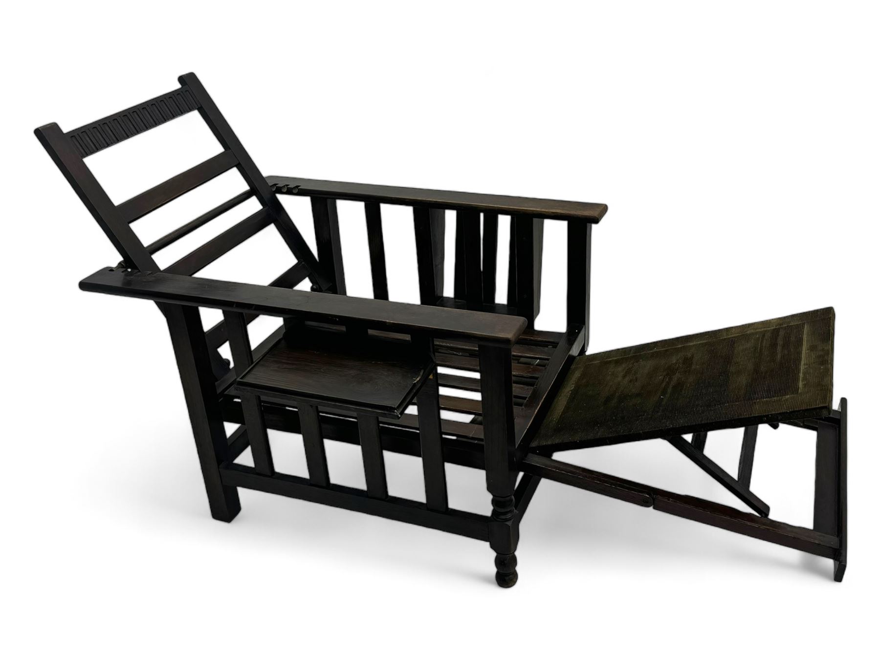 Late Victorian oak steamer chair, adjustable slatted backrest with grooved crest rail, wide armrests extending to a sliding adjustable footrest, open frame sides with vertical slats, side magazine rack and collapsible table, raised on turned front supports