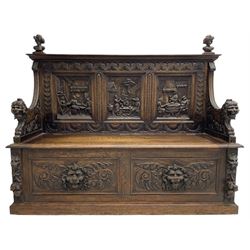19th century heavily carved oak settle, the moulded upper rail over triangular foliage carved frieze, three Flemish style carved panels depicting tavern scenes, acanthus carved uprights terminating to lion carved arms, hinged box seat, the panelled front carved with lion masks and extending scrolled acanthus leaves, on moulded skirt base