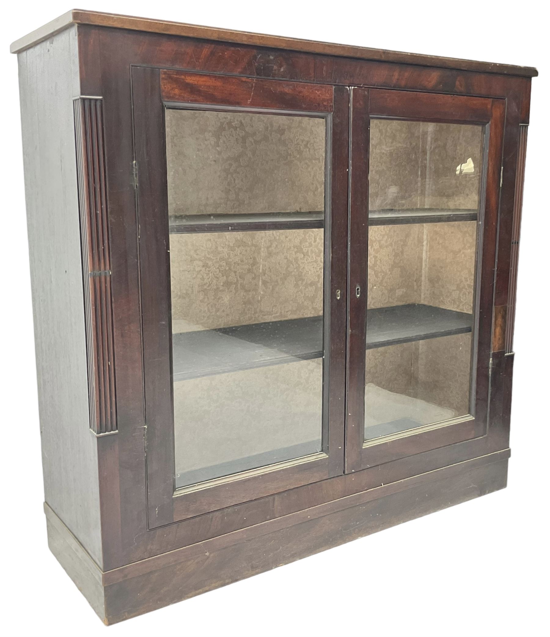 Edwardian mahogany enclosed bookcase, fitted with two glazed doors enclosing two shelves, flanked by reeded uprights, on skirted base