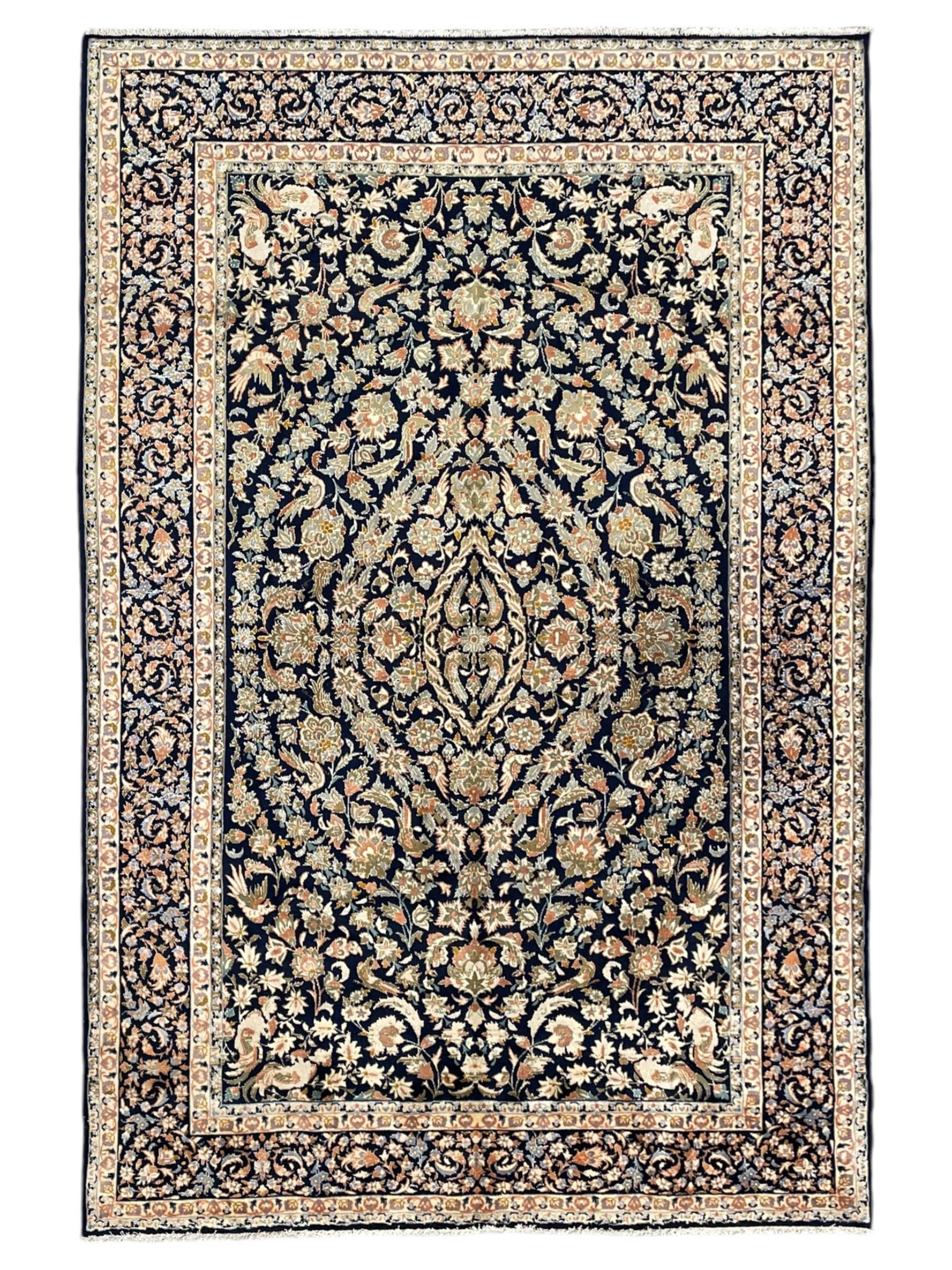 Persian Kashan indigo ground rug, the field consisting of trailing flower head bands and leafy branches, decorated with kuş or bird motifs, the border with repeating border containing curling leaves and flower heads, within guard bands 
